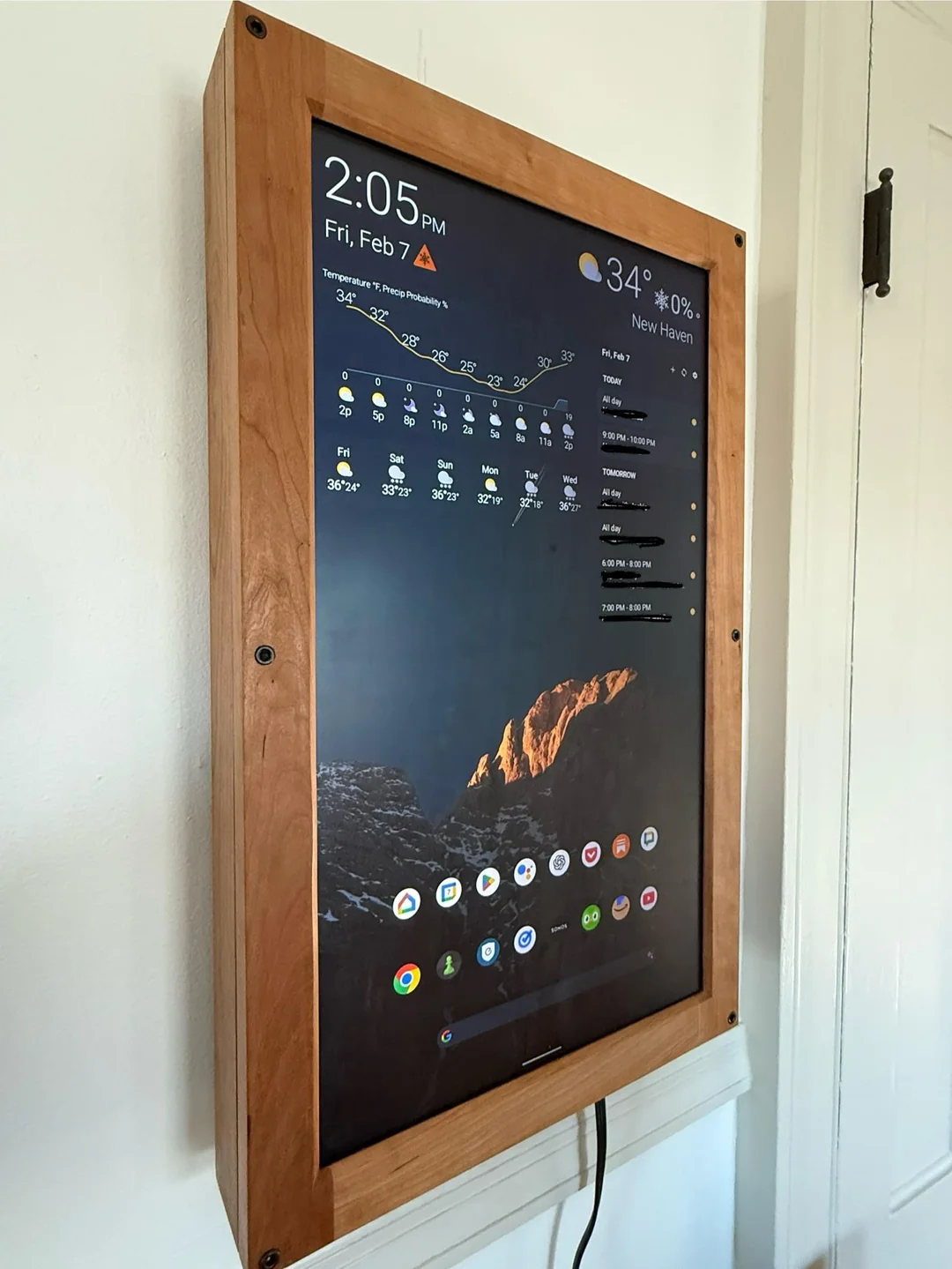 A 24-inch touchscreen home dashboard in a custom wooden enclosure, running an Android-style interface with widgets and app icons.